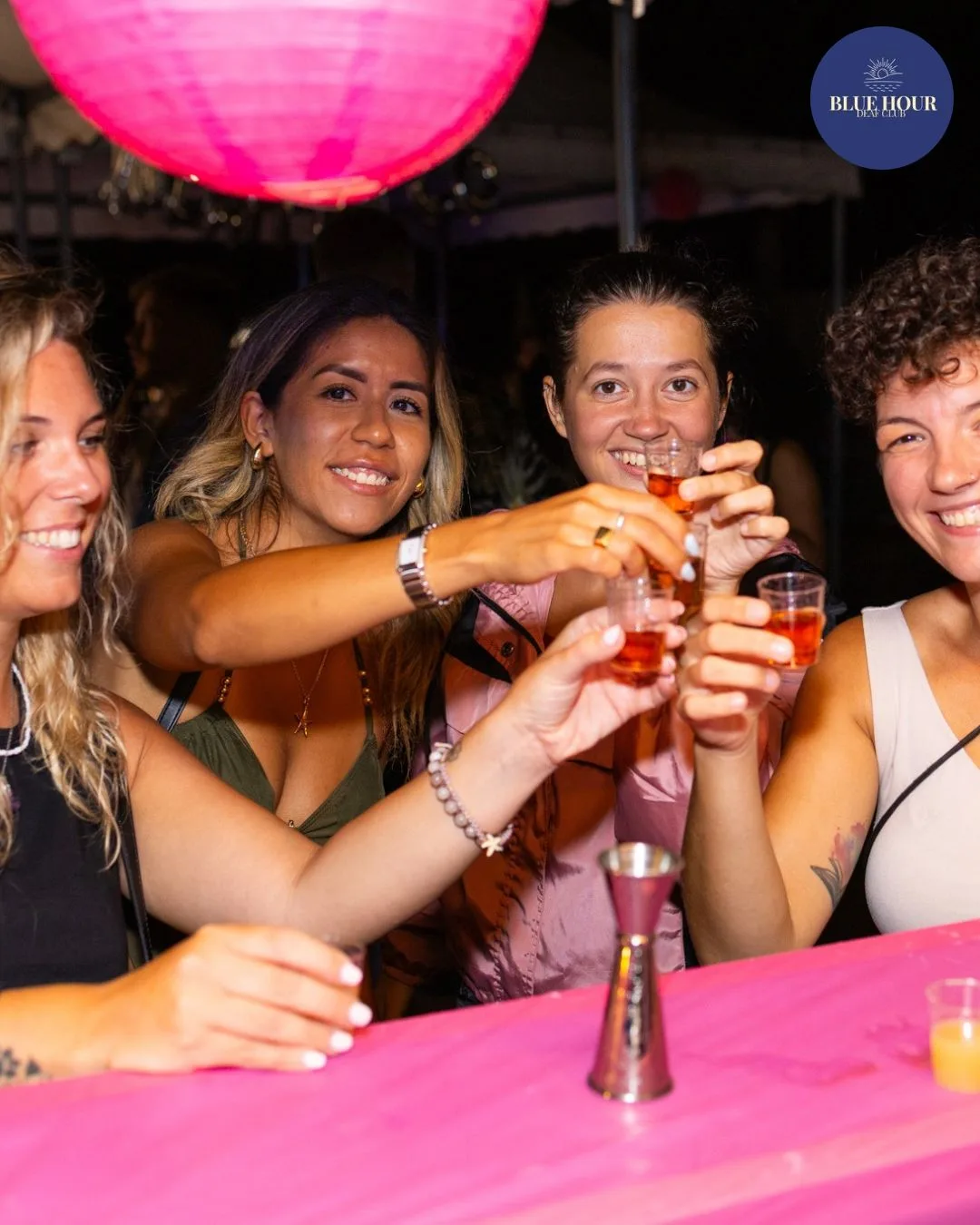 Quattro persone brindano con bicchierini sotto una grande lanterna rosa