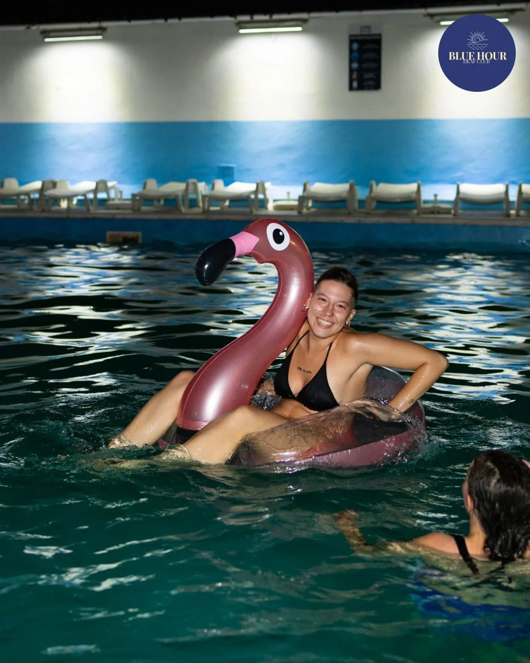 Una persona sorride su un fenicottero gonfiabile rosa nella piscina illuminata di notte