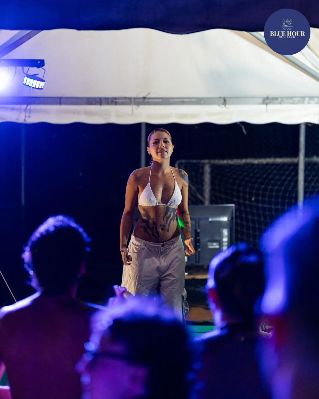 Una performer sul palco sotto il tendone, vista dal pubblico immerso nella luce blu